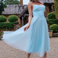Elegant woman wearing a light blue tulle midi dress with a satin bodice, posing gracefully in a romantic garden setting.