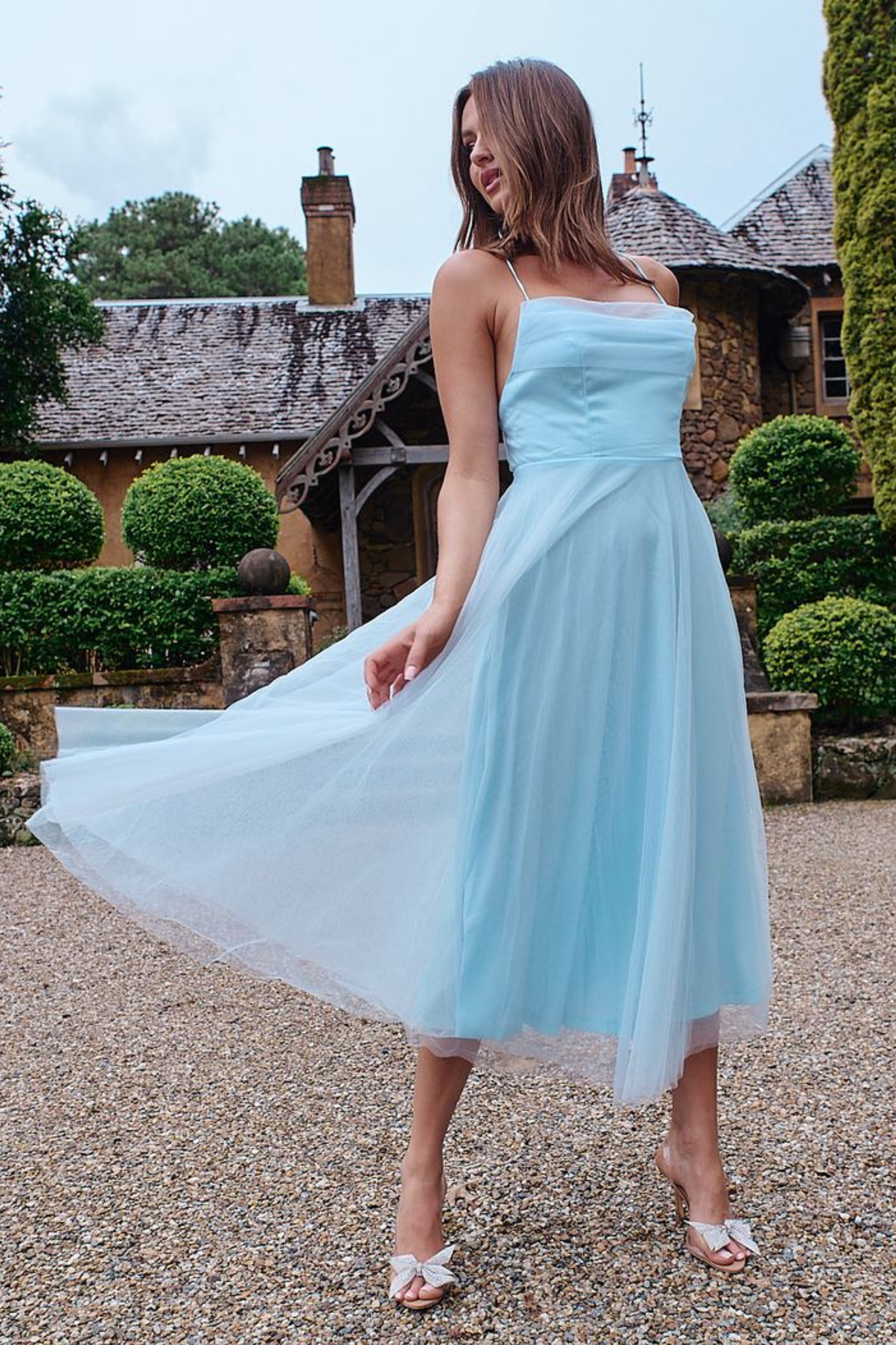 Elegant woman wearing a light blue tulle midi dress with a satin bodice, posing gracefully in a romantic garden setting.